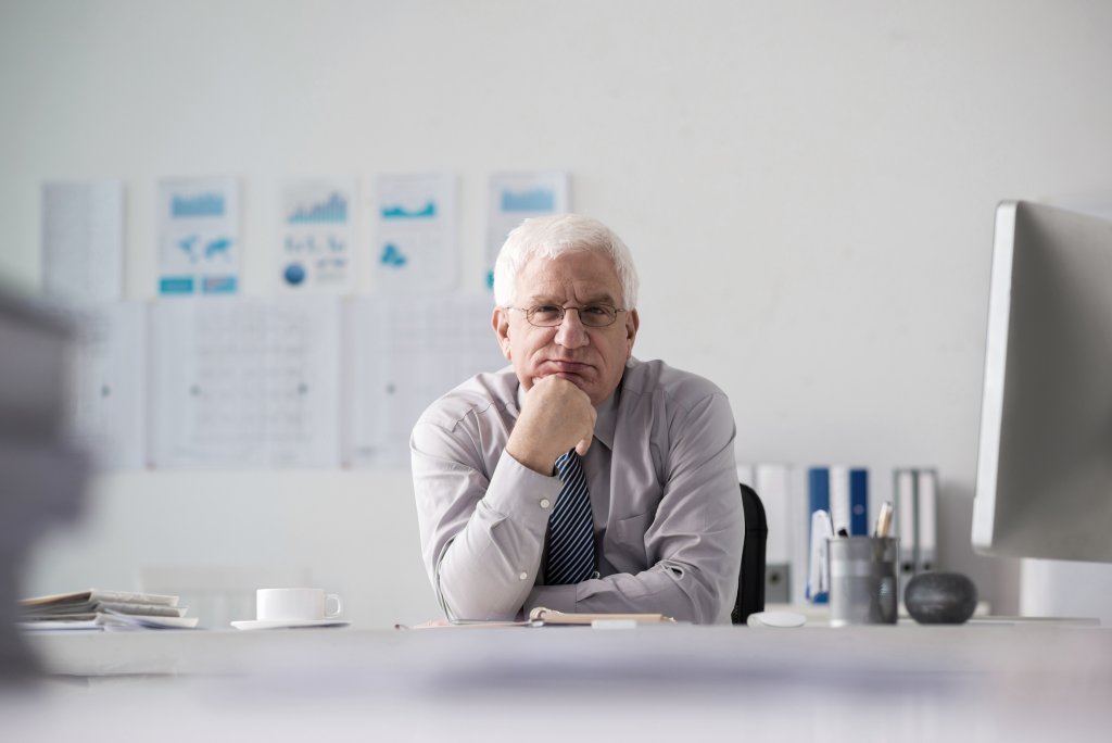 Pensive senior entrepreneur looking at camera when sitting at table